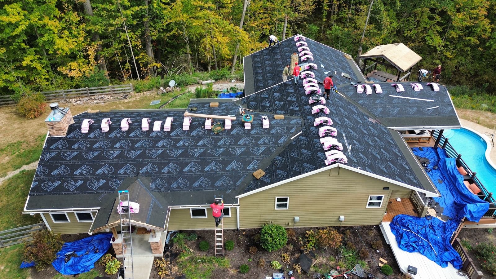 Row of steep gabled dormers with tan asphalt shingle roofs and metal flashing against a clear blue sky
